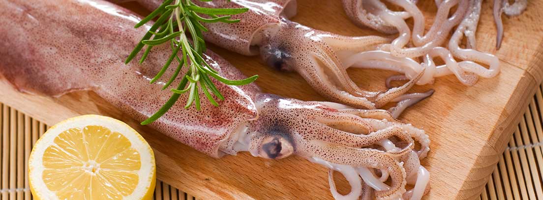 Calamares frescos en una tabla de madera junto a un cuchillo y un limón