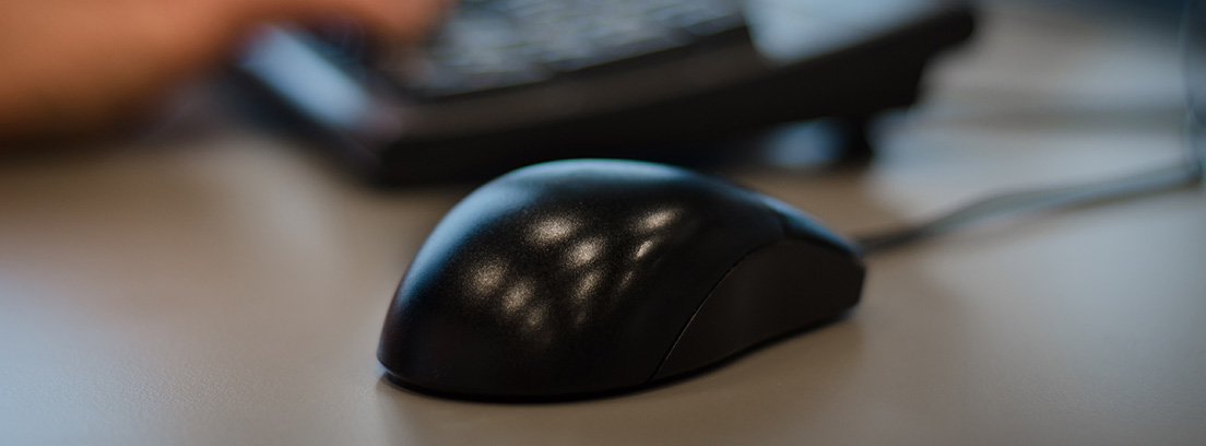 Ratón de color negro y con cable junto a teclado de ordenador.