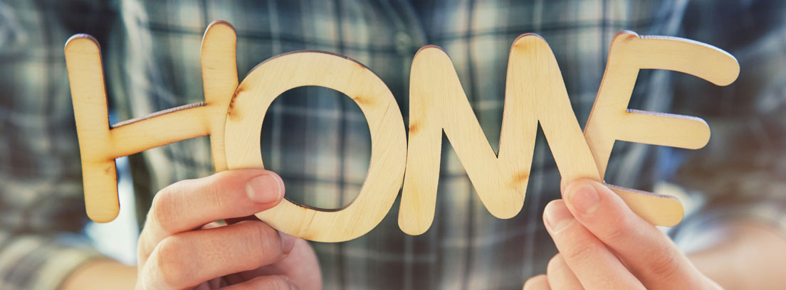 Manos sujetando unas letras de madera formando la palabra “home”