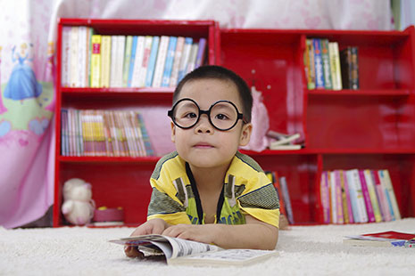 Niño con gafas redondas tumbado en el suelo con un libro abierto entre sus manos