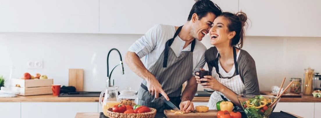 Una mujer y un hombre se sonríen mientras preparan unas pizzas