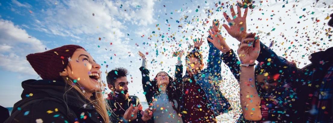 Seis jóvenes con semblante festivo levantan los brazos bajo una nube de confeti