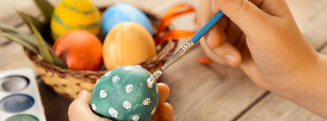 Una niña pinta un huevo con colores y pincel