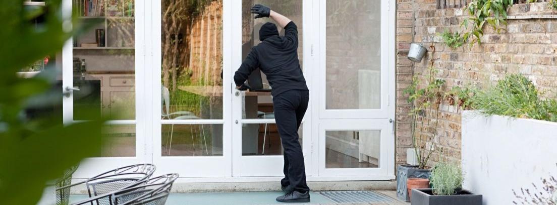 Hombre vestido de negro intentando forzar la puerta de una casa