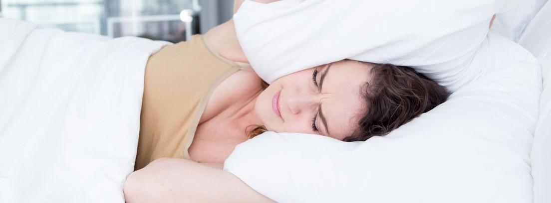 mujer tapándose los oídos con una almohada por causa del ruido