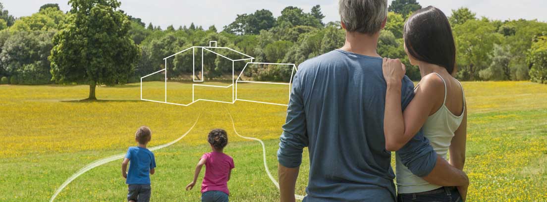 Hombre y mujer de espaldas abrazados observando un terreno con líneas dibujadas que forman una casa, y dos niños corriendo delante de ellos.
