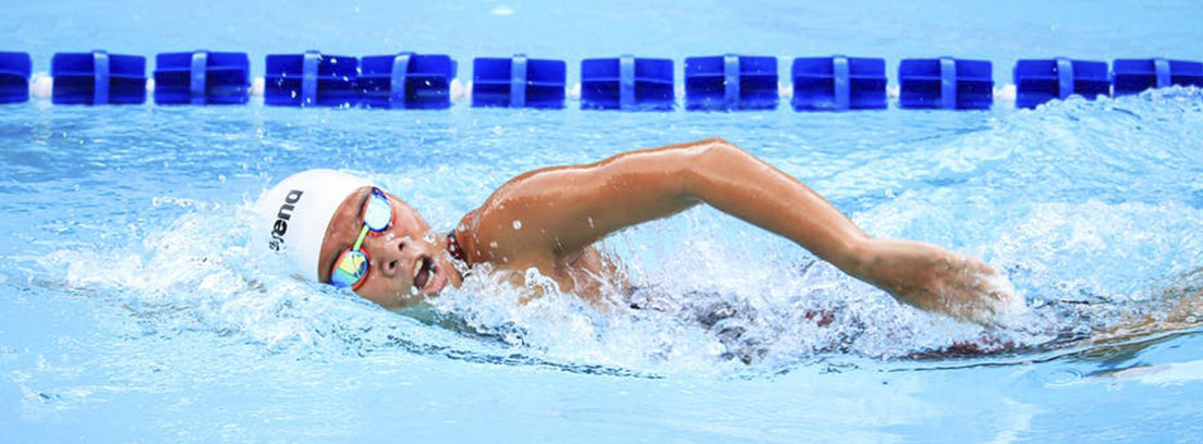 Persona con gorro y gafas de nadar dentro de una piscina nadando