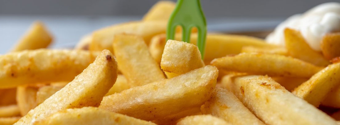Tenedor de plástico pinchando patatas fritas, un tipo de alimento precocinado considerado malo
