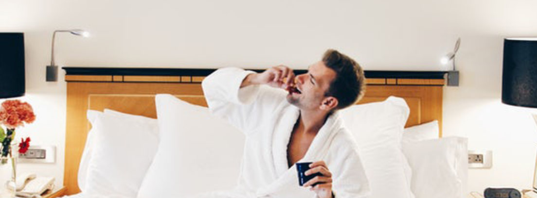Hombre en cama de habitación de hotel comiendo y bebiendo