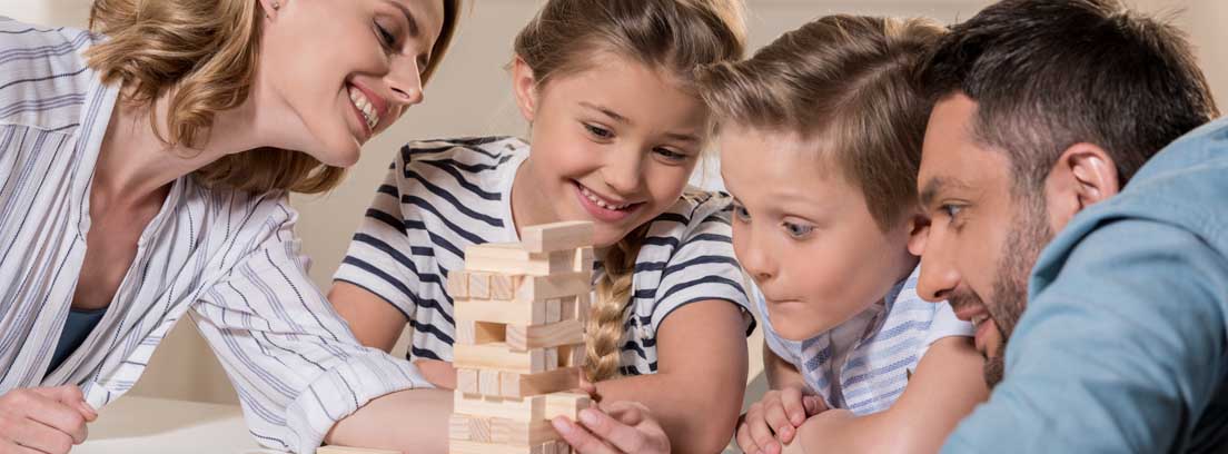 Dos adultos y don niños sonriente alrededor de una mesa disfrutando de uno de los mejores juegos para jugar en familia en casa