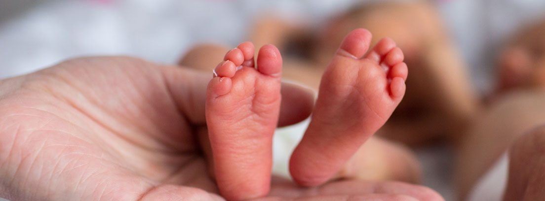 Mano de mujer sujetando los pies de un bebé prematuro