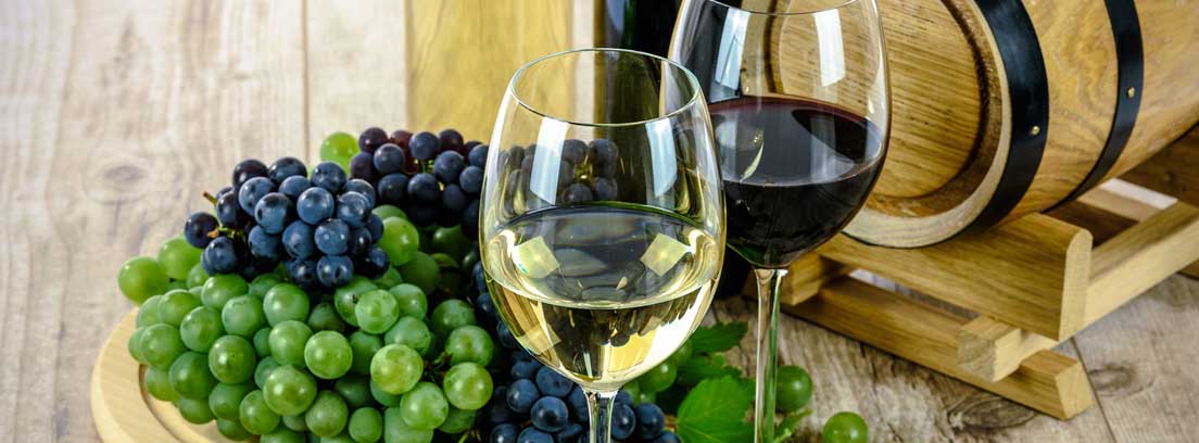 Dos copas de vino tinto y blanco sobre una mesa con uvas