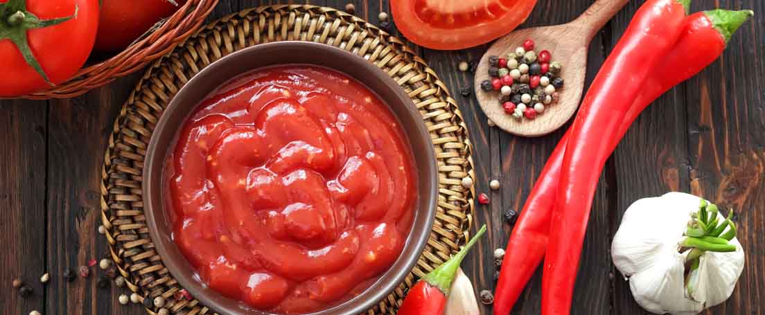 Cuenco con salsa de tomate junto a tomates, guindilla, pimienta y ajo