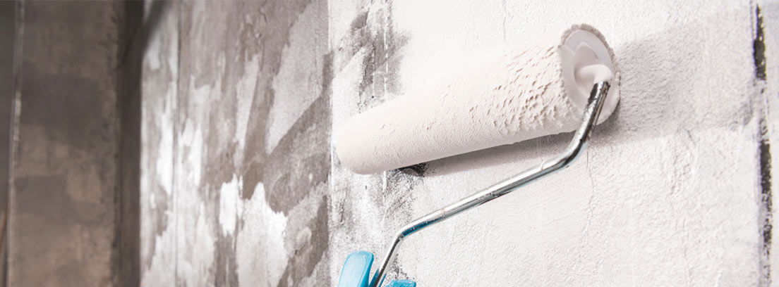 Mano con rodillo pintando pared en color blanco