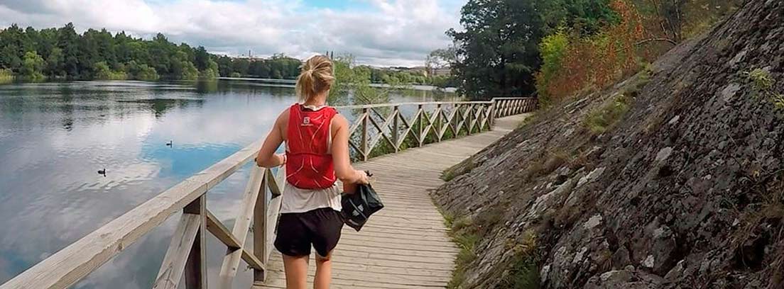 Mujer corriendo junto a un lago con bolsa de basura en la mano.