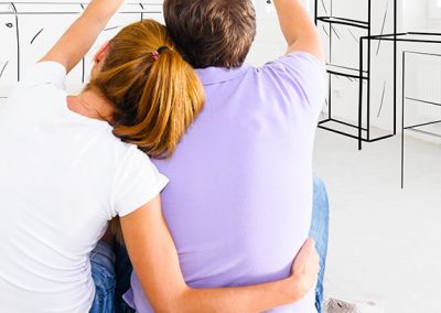 Hombre y mujer sentados de espalda miran paredes blancas con dibujos de muebles
