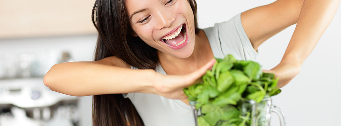 Mujer sonriente introduciendo verduras en una batidora