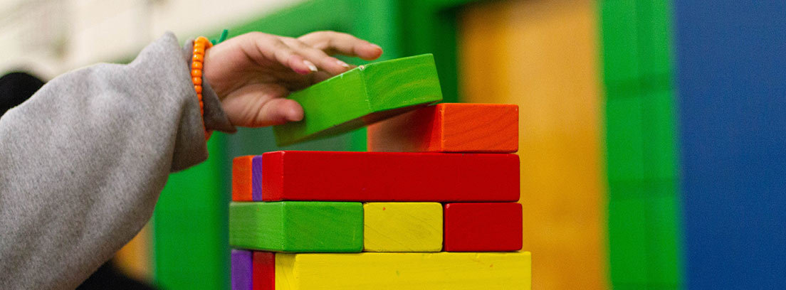 Mano de niño poniendo pieza de madera en torre de bloques de colores