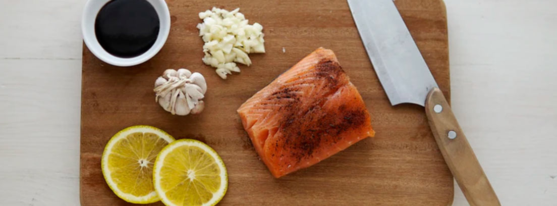 Lomo de salmón junto a dos rodajas de limón y un cuchillo sobre una tabla de madera