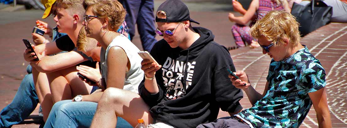 Varios adolescentes sentados al aire libre mirando sus teléfonos móviles