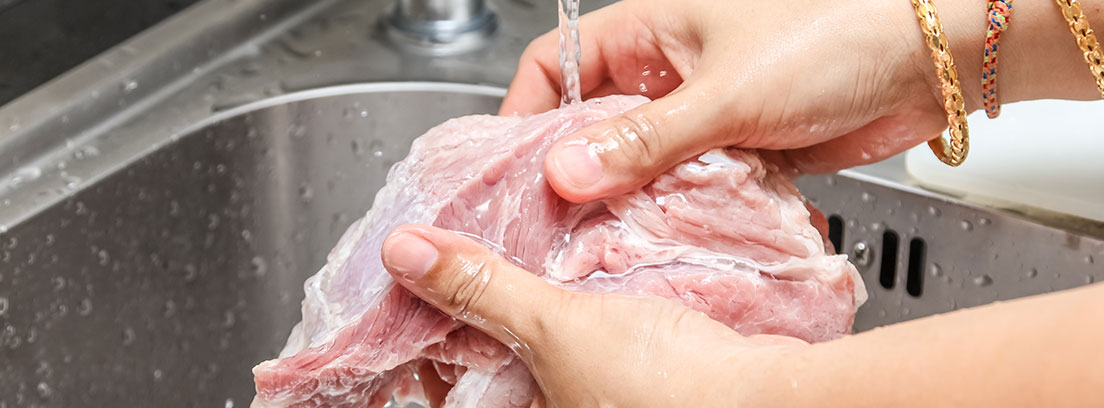 Primer plano de unas manos lavando un trozo de carne cruda bajo el grifo