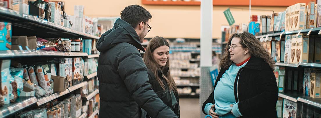 Un hombre y dos mujeres junto a carro de la compra en un pasillo de supermercado.