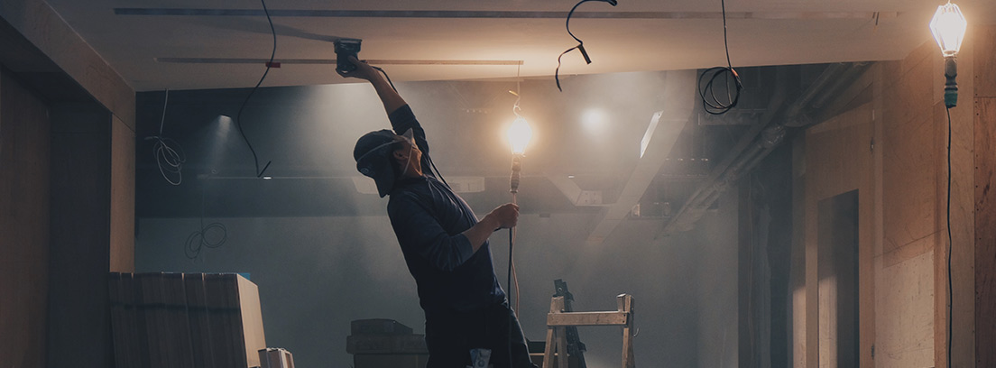 Hombre subido a escalera con mano en el techo de una habitación en obras.