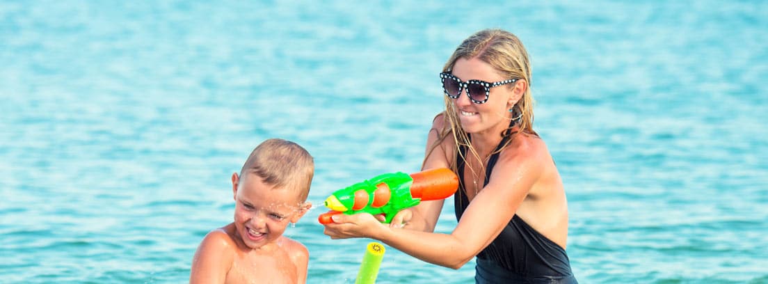 Madre e hijo jugando con pistolas de agua en la playa
