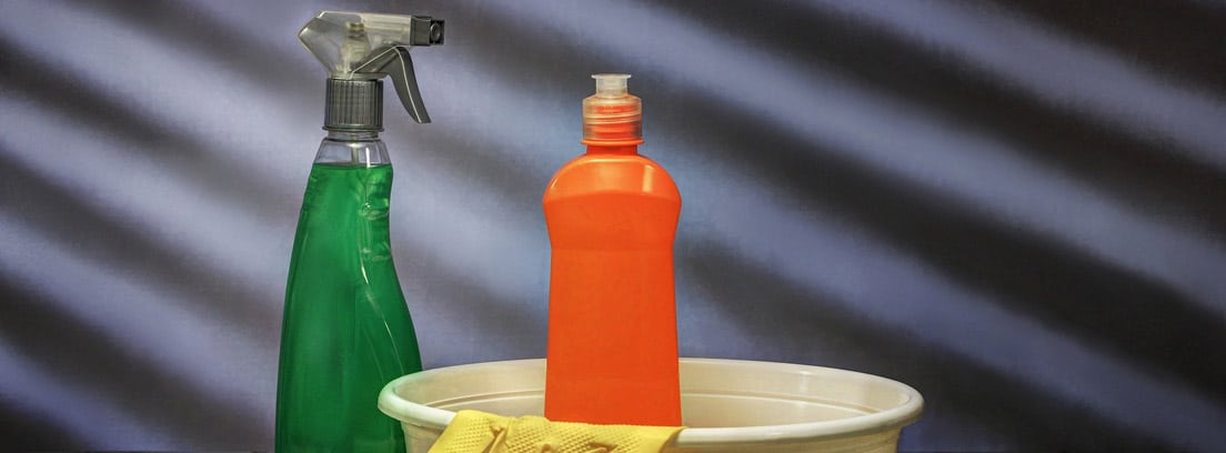 Productos de limpieza en un balde junto a un estropajo y unos guantes. 