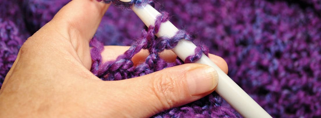 Manos realizando crochet con una lana morada