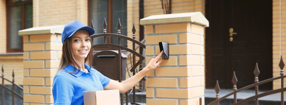 Mujer con gorra azul y paquetes en la mano llamando al timbre de una casa
