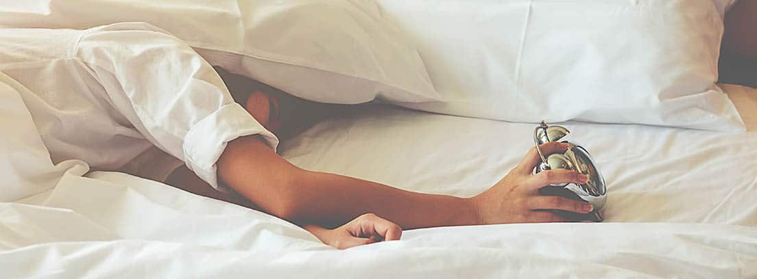 Hombre durmiendo sobre un colchón apagando un despertador
