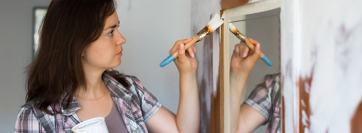 Mujer con una paletina pintando un armario de blanco