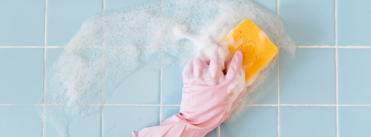 Persona limpiando azulejos con jabón y estropajo