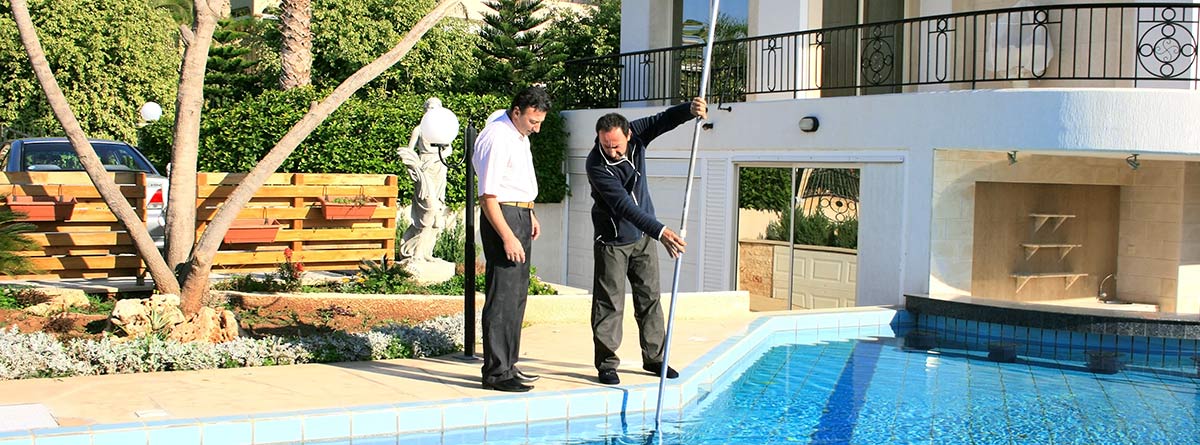 Dos hombres junto a una piscina usando un limpiafondos
