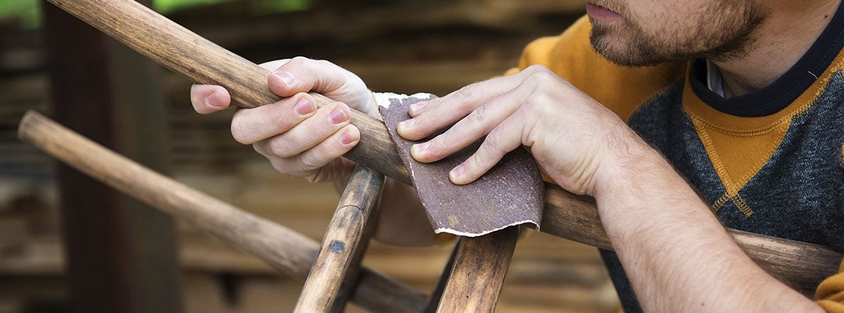 unas manos lijando las patas de una silla de madera