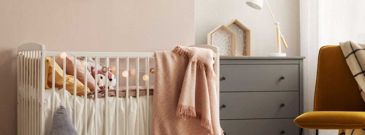 habitación de bebé con la pared rosa palo y cajonera gris