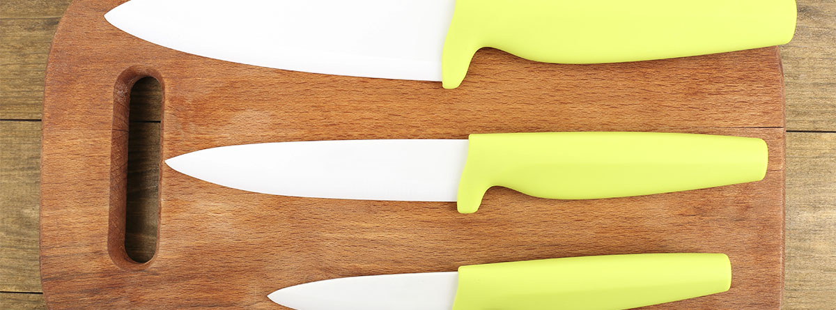 Cuchillos cerámicos de distintos tamaños con el mango de color amarillo sobre una tabla de madera.