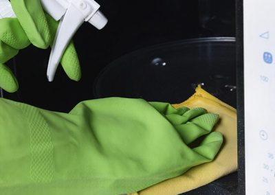 Manos con guantes limpiando un microondas con un spray y una paño