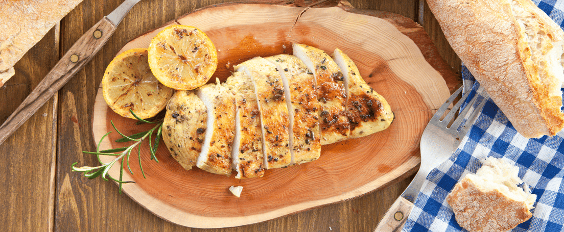 pollo-al-limon Vista cenital de una mesa con un plato con pechuga de pollo troceada y rodajas de limón, cuenco con sopa, pan y cubiertos