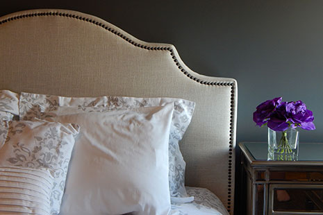 Cabecero forrado de tela con almohadones y mesita de noche con flores moradas