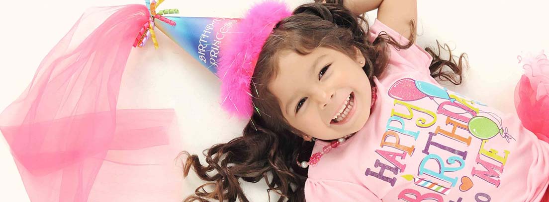 Niña sonriente con gorro de cumpleaños y camiseta en la que se lee: “Happy birthday to me”