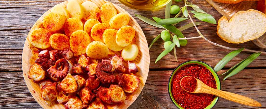 Receta de pulpo a la gallega Vista cenital de un plato de pulpo a la gallega y patatas y un cuenco con pimentón