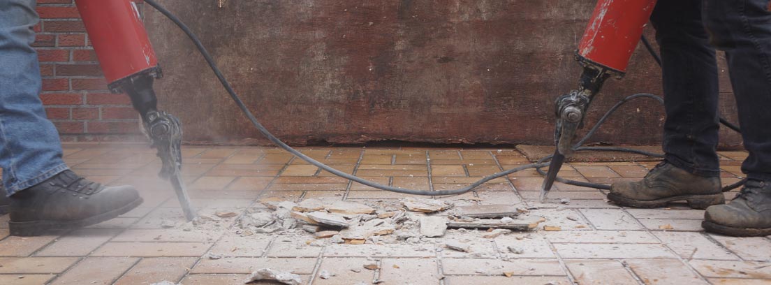 Don hombres con martillos demoledores quitando el suelo de una vivienda por una avería general