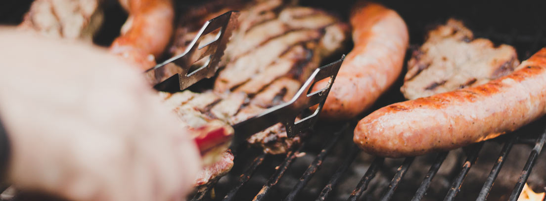 Primer plano de una mano sujetando carne en la barbacoa con unas pinzas