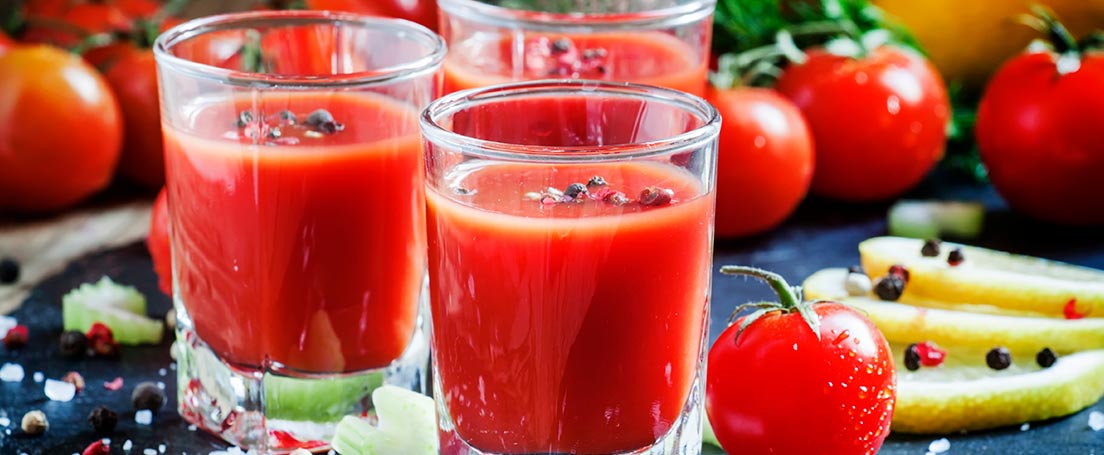 Varios vasos con cóctel Bloody Mary junto a tomates.