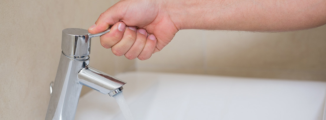 Mano abriendo el grifo de un baño